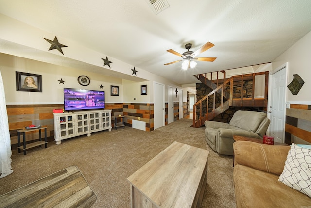 carpeted living room with ceiling fan, a textured ceiling, and wooden walls