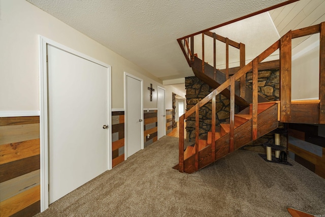 stairs featuring carpet flooring, wood walls, and a textured ceiling