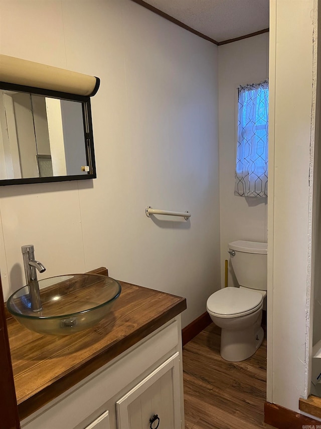 bathroom with hardwood / wood-style floors, vanity, toilet, ornamental molding, and a textured ceiling