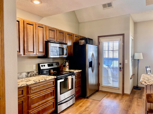 kitchen featuring lofted ceiling, light wood-type flooring, a textured ceiling, light stone counters, and stainless steel appliances