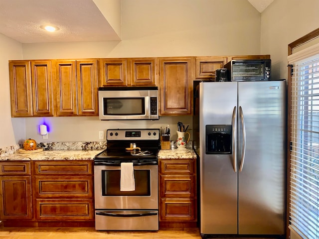 kitchen with light stone counters, light hardwood / wood-style floors, a textured ceiling, and appliances with stainless steel finishes