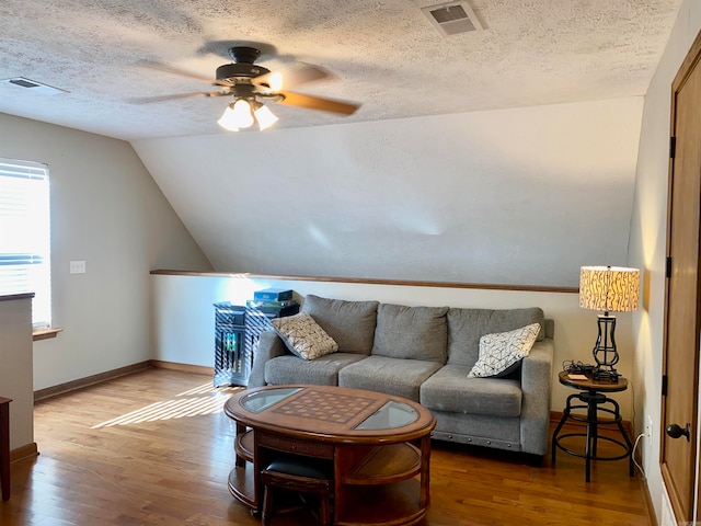 living room with ceiling fan, wood-type flooring, a textured ceiling, and vaulted ceiling