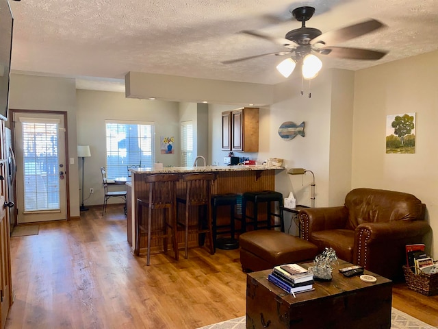 living room with a textured ceiling, light wood-type flooring, ceiling fan, and sink