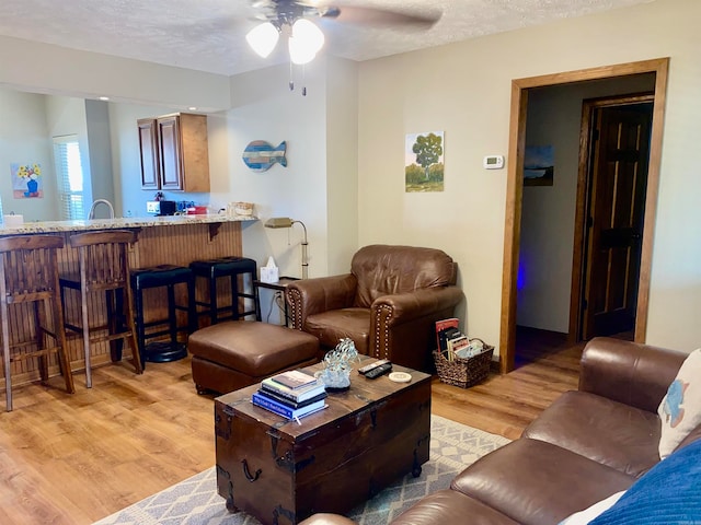 living room featuring ceiling fan, sink, light wood-type flooring, and a textured ceiling