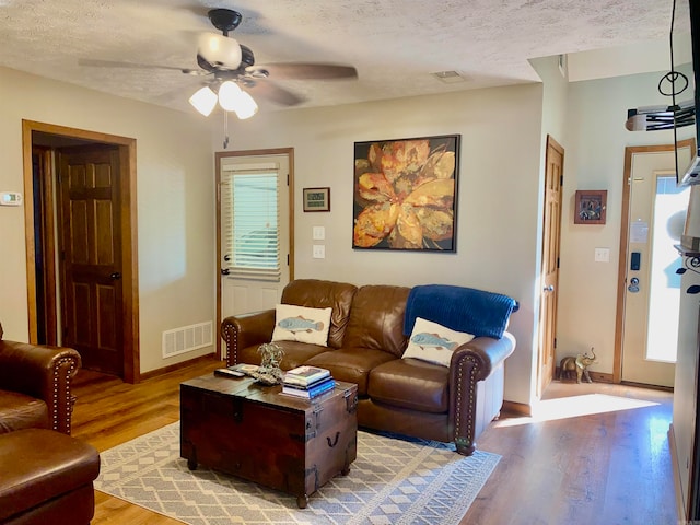 living room with a textured ceiling, light hardwood / wood-style floors, and ceiling fan