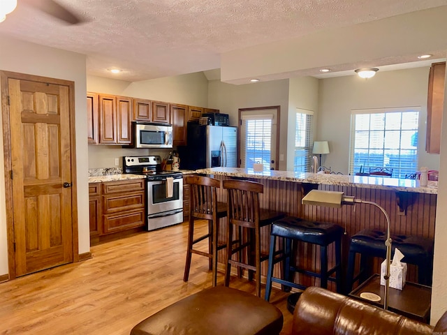 kitchen featuring a kitchen breakfast bar, stainless steel appliances, a textured ceiling, and light hardwood / wood-style floors