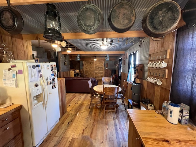 kitchen featuring white refrigerator with ice dispenser, light wood-type flooring, and wood walls