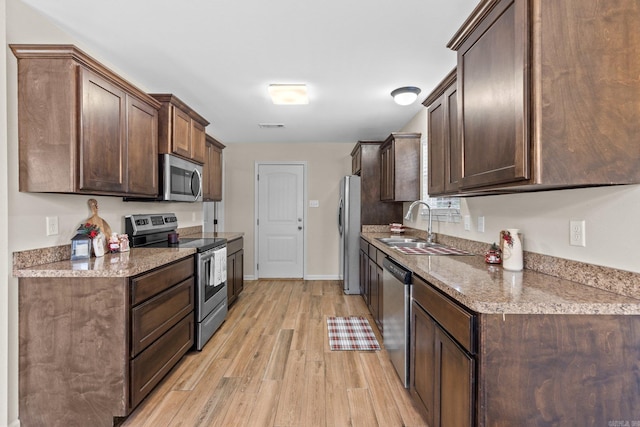 kitchen featuring dark brown cabinetry, sink, light stone counters, light hardwood / wood-style flooring, and appliances with stainless steel finishes