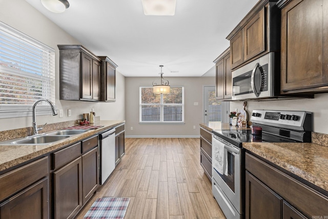 kitchen with dark brown cabinetry, sink, stainless steel appliances, decorative light fixtures, and light wood-type flooring