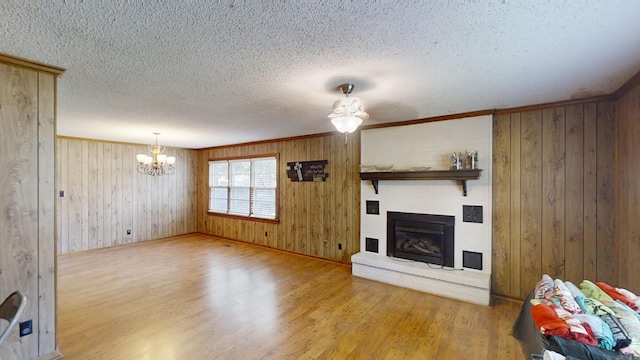 unfurnished living room with wood walls, wood-type flooring, a textured ceiling, and an inviting chandelier