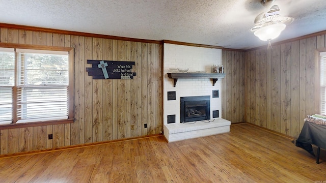 unfurnished living room featuring a textured ceiling, hardwood / wood-style flooring, a brick fireplace, and wood walls