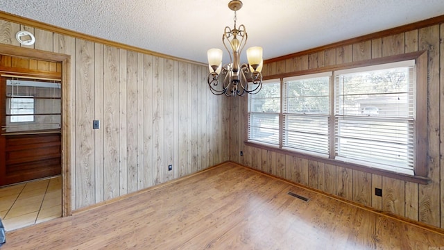 unfurnished dining area with hardwood / wood-style floors, wood walls, and an inviting chandelier