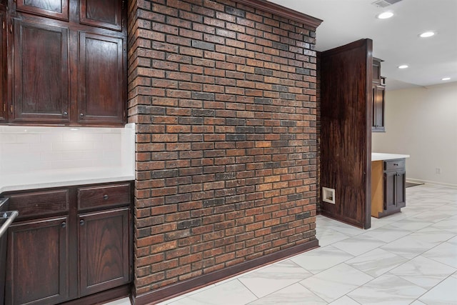 kitchen featuring tasteful backsplash, dark brown cabinets, and brick wall