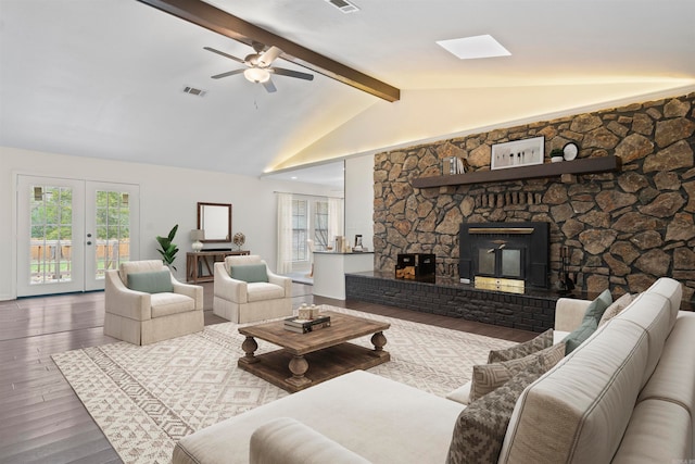 living room with ceiling fan, french doors, vaulted ceiling with beams, a stone fireplace, and hardwood / wood-style floors