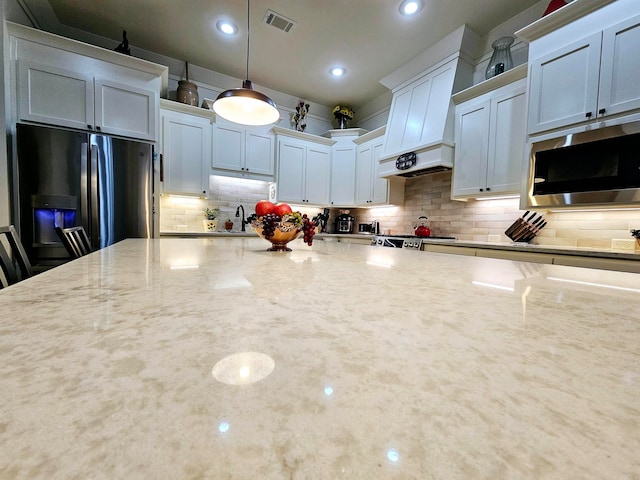 kitchen with white cabinetry, light stone countertops, stainless steel appliances, backsplash, and decorative light fixtures