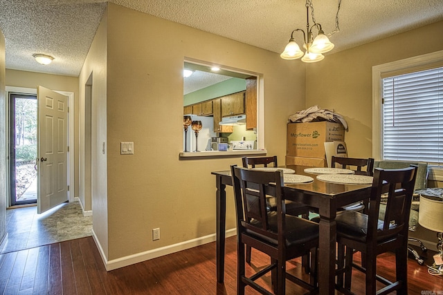 dining space featuring a textured ceiling, dark hardwood / wood-style flooring, a healthy amount of sunlight, and a notable chandelier