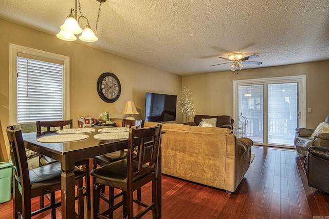 dining area with ceiling fan with notable chandelier, dark wood-type flooring, and a textured ceiling