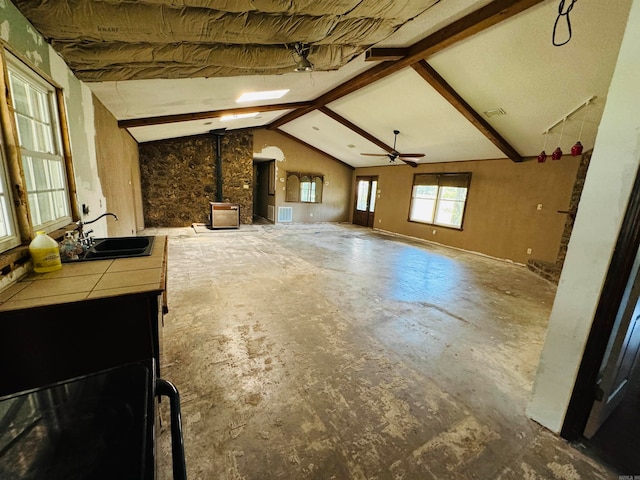 living room with a wood stove, ceiling fan, sink, and lofted ceiling with beams