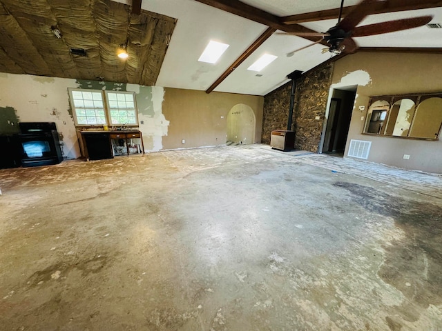 interior space featuring ceiling fan, high vaulted ceiling, beamed ceiling, concrete floors, and a wood stove