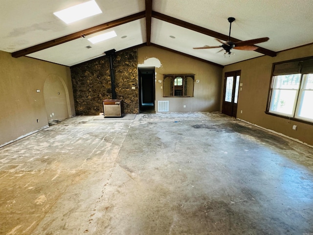 unfurnished living room with a wood stove, ceiling fan, a textured ceiling, and vaulted ceiling with beams