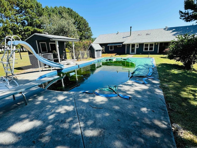 view of swimming pool featuring a storage unit, a lawn, and a water slide