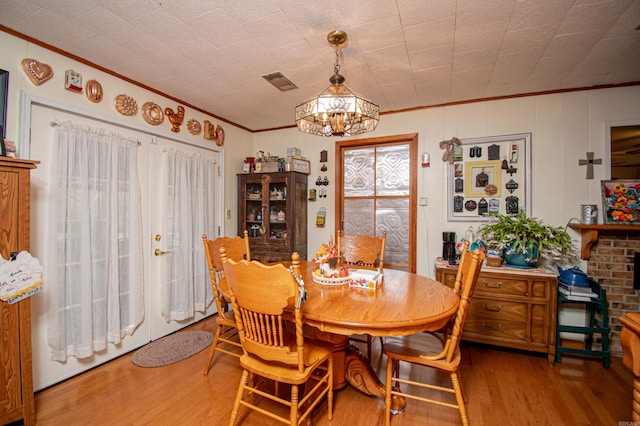 dining area with wood-type flooring, a healthy amount of sunlight, ornamental molding, and a notable chandelier