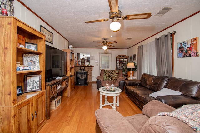 living room featuring ornamental molding, a textured ceiling, ceiling fan, light hardwood / wood-style floors, and a wood stove