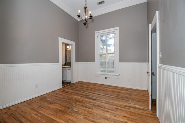 empty room with hardwood / wood-style floors, ornamental molding, and an inviting chandelier