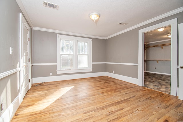 unfurnished bedroom with a closet, a walk in closet, a textured ceiling, and light hardwood / wood-style flooring