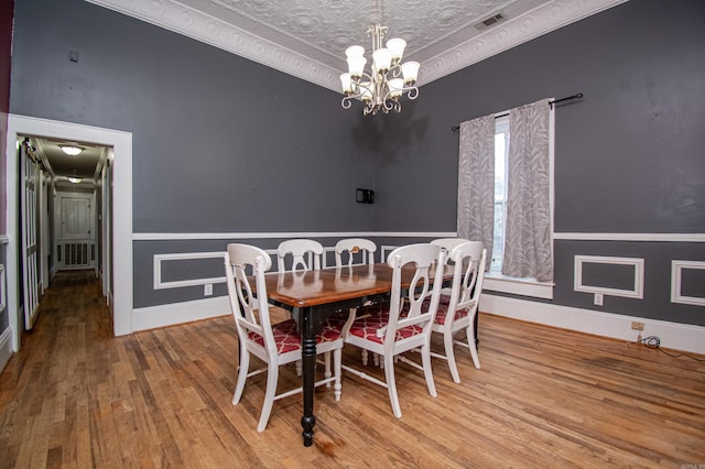 dining room featuring wood-type flooring, ornamental molding, and an inviting chandelier