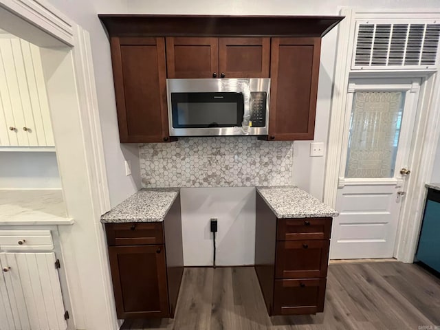 kitchen featuring light stone counters, stainless steel microwave, dark wood finished floors, and decorative backsplash