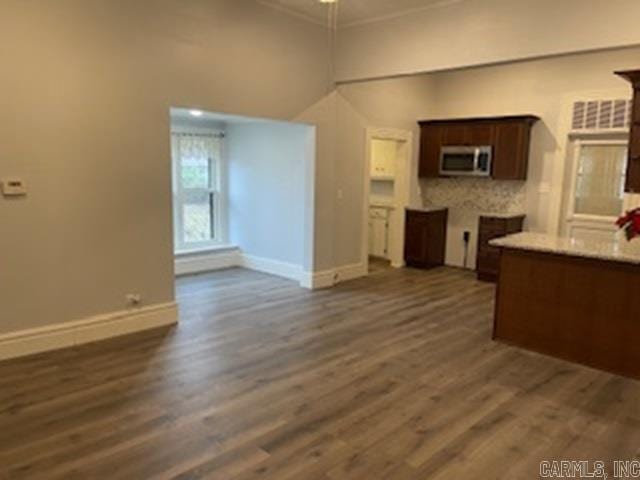 kitchen featuring dark brown cabinetry, baseboards, dark wood finished floors, stainless steel microwave, and ornamental molding