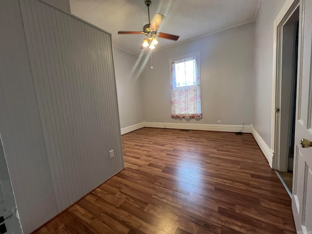 empty room featuring crown molding, wood finished floors, a ceiling fan, and baseboards