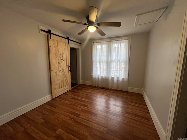 unfurnished bedroom with a barn door, a ceiling fan, baseboards, dark wood-style floors, and attic access