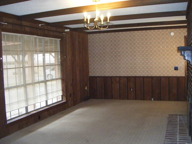 carpeted empty room featuring wood walls and an inviting chandelier