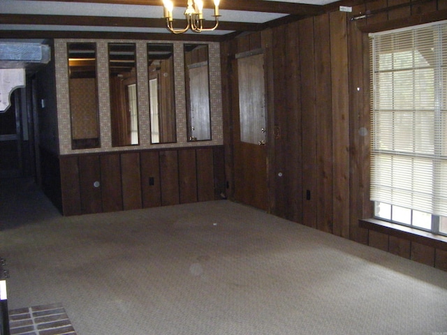 spare room with carpet floors, a wealth of natural light, a notable chandelier, and wood walls