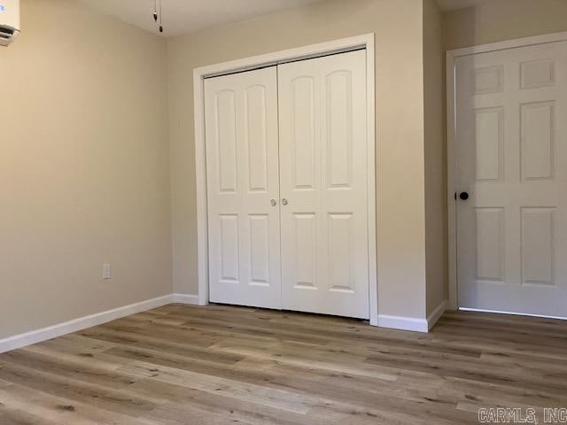 unfurnished bedroom with a wall mounted AC, light hardwood / wood-style floors, and a closet