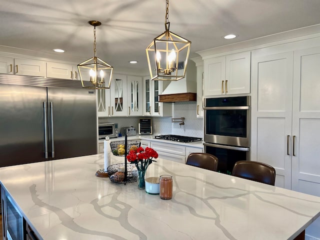 kitchen with white cabinets, stainless steel appliances, light stone counters, and hanging light fixtures