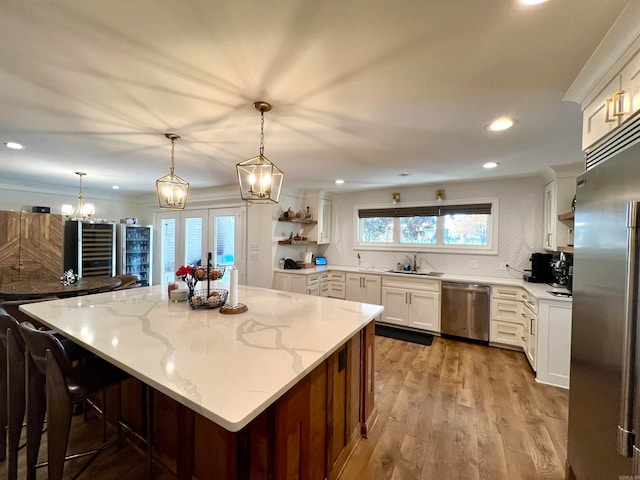 kitchen featuring hanging light fixtures, light wood-type flooring, light stone counters, white cabinetry, and stainless steel appliances