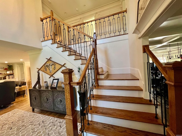 stairs featuring a high ceiling, hardwood / wood-style flooring, and crown molding