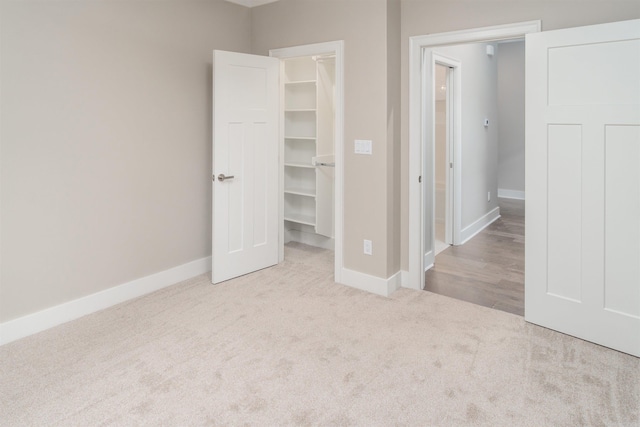 unfurnished bedroom with a spacious closet, a closet, and light colored carpet