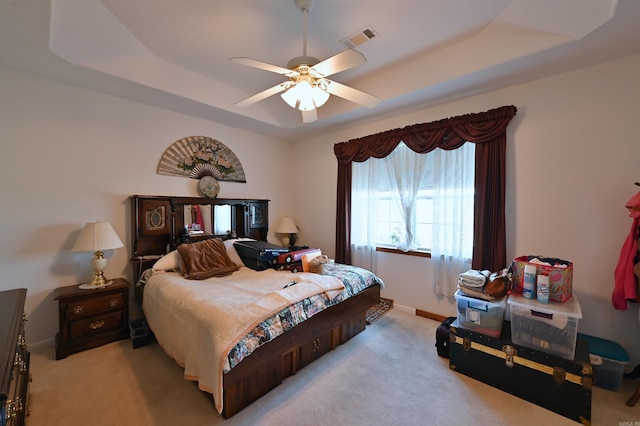 bedroom featuring ceiling fan, light colored carpet, and a tray ceiling