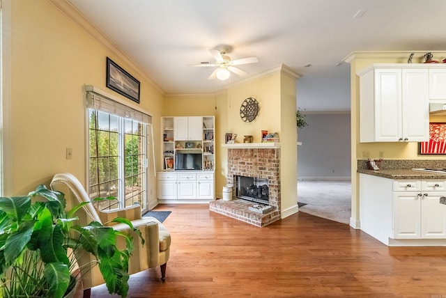 living room with ceiling fan, light wood-type flooring, crown molding, and a brick fireplace