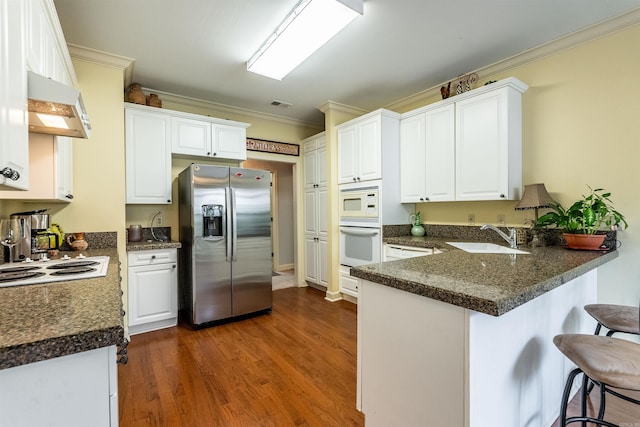 kitchen with white cabinetry, sink, range hood, kitchen peninsula, and white appliances