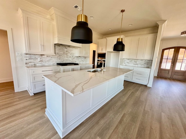 kitchen with french doors, tasteful backsplash, a kitchen island with sink, sink, and white cabinets