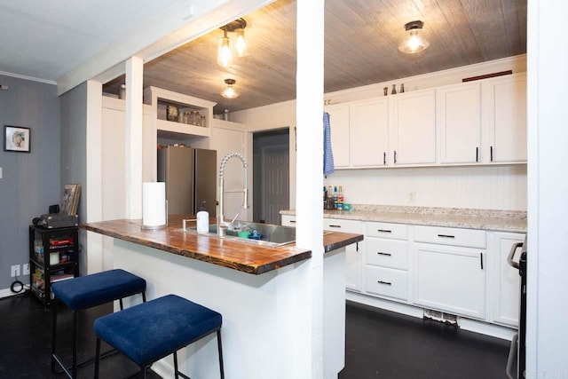 kitchen with a breakfast bar, white cabinets, stainless steel refrigerator, butcher block counters, and wood ceiling