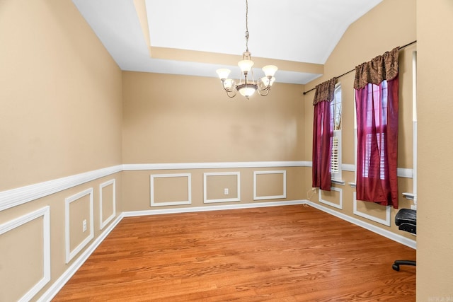 empty room with hardwood / wood-style floors, a notable chandelier, and vaulted ceiling