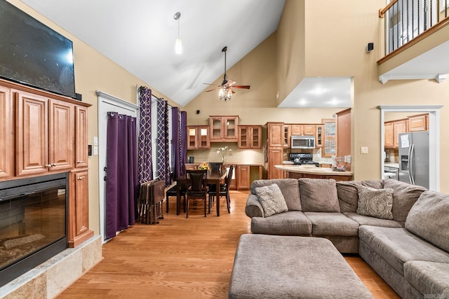 living room with ceiling fan, light hardwood / wood-style floors, a premium fireplace, and high vaulted ceiling