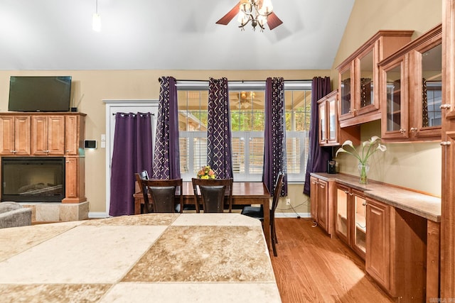 dining space featuring a tile fireplace, ceiling fan, light hardwood / wood-style flooring, and vaulted ceiling