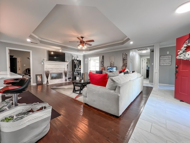 living room featuring ceiling fan, a raised ceiling, wood-type flooring, and a premium fireplace